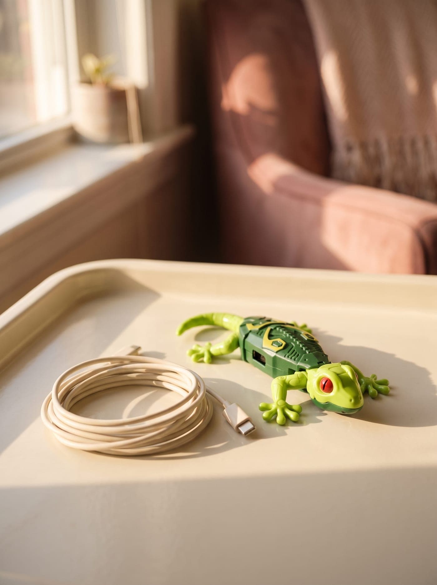 The gecko resting on a side table next to a coiled USB-C charging cable